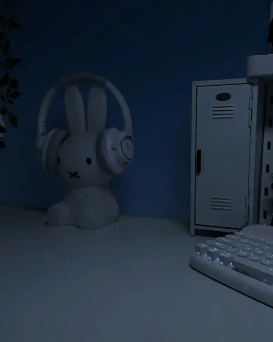 Decoración aesthetic para setup de escritorio minimalista con accesorios blancos, figura de conejo con auriculares y teclado mecánico bajo luz tenue.